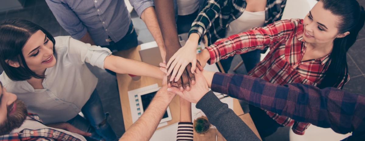 Team gathering one hand in the center of a circle, symbolizing teamwork