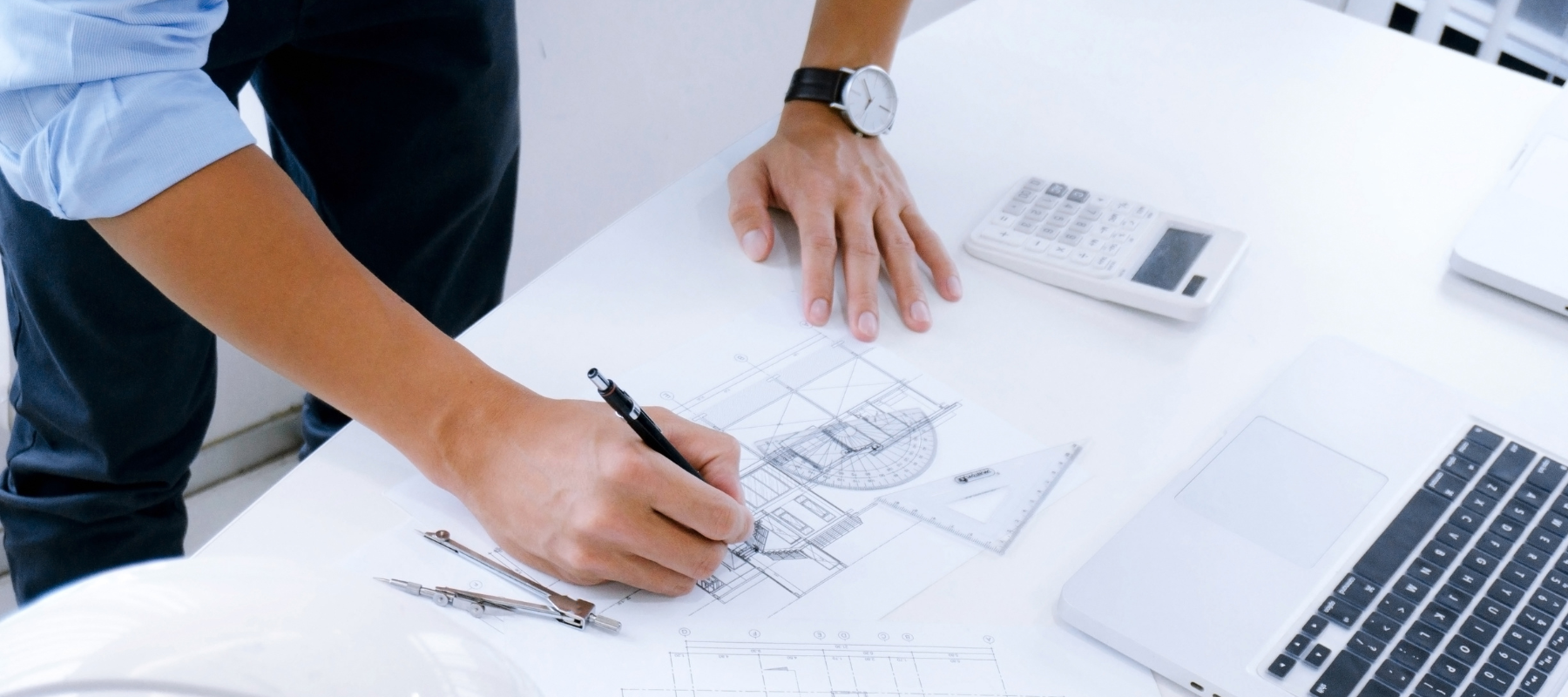 Close up of Architect's hands drawing plans, with laptop on desk