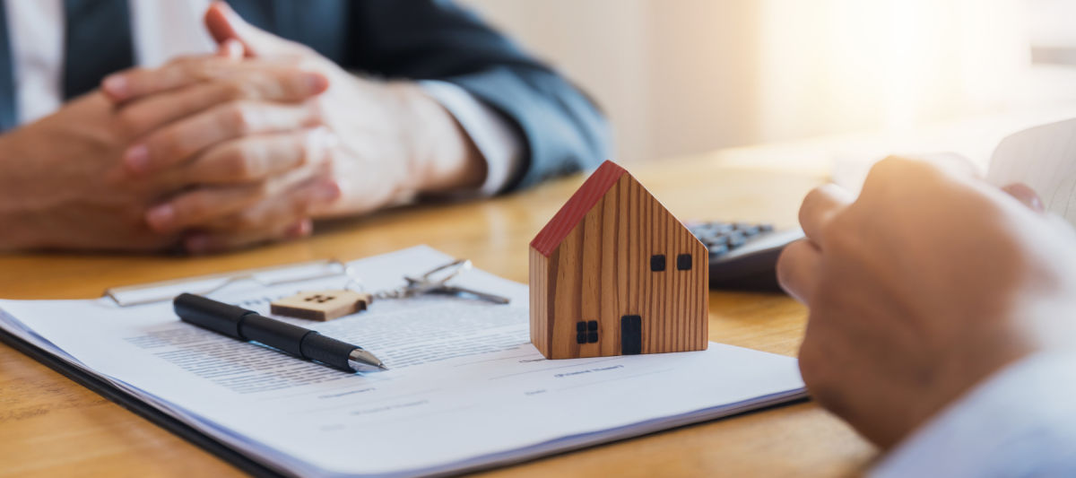 Real Estate concept, small wooden house and keys on top of document with realtor and client at a table