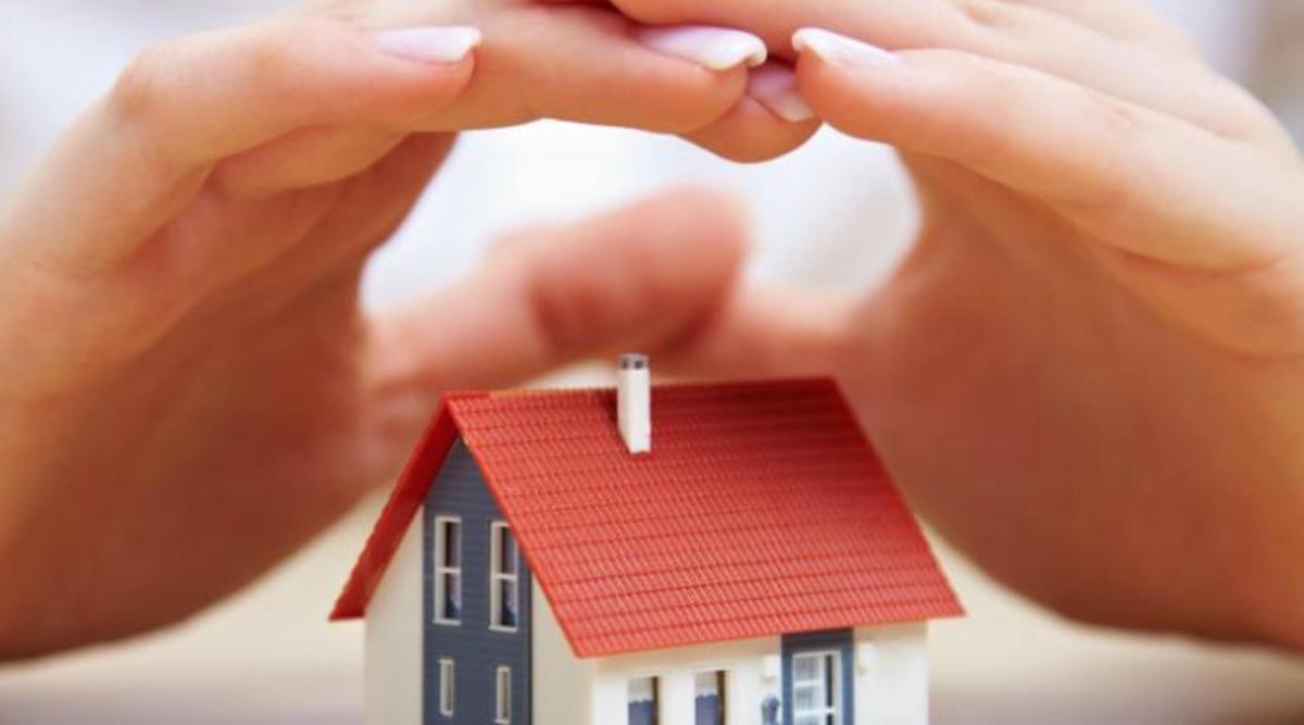 Hands protecting a small toy house, symbolizing the Insurance industry